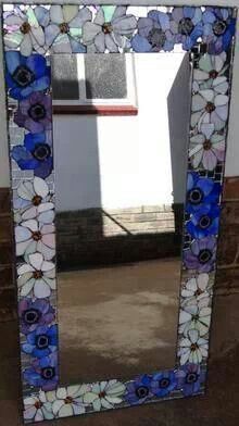 a mirror that has flowers on it in front of a wall with a window behind it