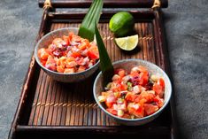 two bowls filled with food sitting on top of a wooden tray next to limes