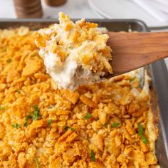 a wooden spoon scooping out some food from a casserole in a pan