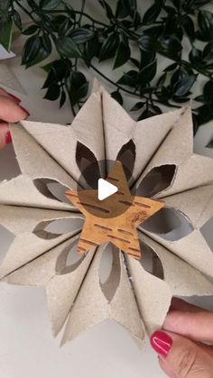 two hands holding up an origami flower on top of a white table next to a potted plant