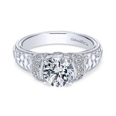 a white gold engagement ring with diamonds on the sides and an intricate band around it