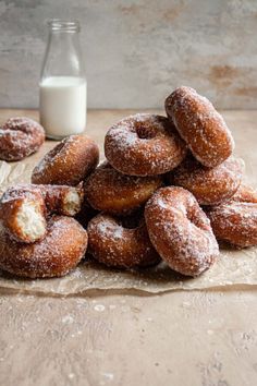 a pile of doughnuts sitting on top of a table next to a bottle of milk