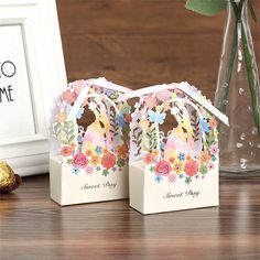 two small gift bags sitting on top of a table next to a vase filled with flowers