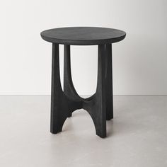 a black round table sitting on top of a white floor next to a gray wall