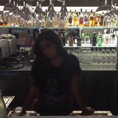 a woman sitting at a bar with lots of liquor bottles in the backgroud