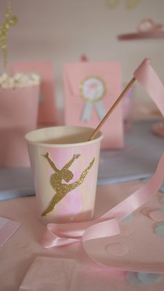 a pink cup with a gold ballerina on it and some decorations around the table