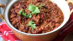 a pot filled with chili and garnish sitting on top of a wooden cutting board