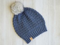 a blue knitted hat with a white pom - pom sits on a wooden floor