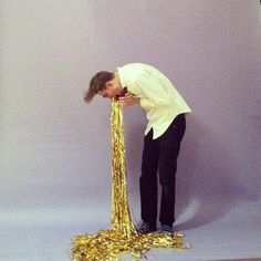 a man in white shirt and black pants leaning over a pile of gold confetti