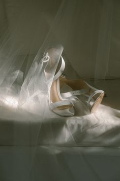 a pair of white high heel shoes sitting on top of a bed under a veil