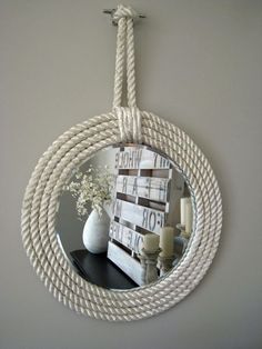 a round mirror hanging on a rope next to a vase