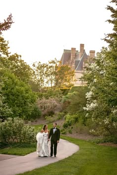 a bride and groom walking down a path in front of a large castle like building