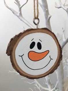 a wood slice with a painted snowman face on it hanging from a tree branch