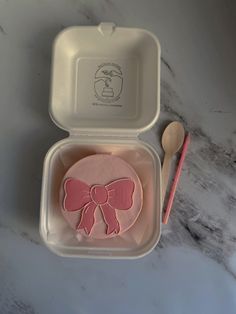 a pink bow shaped cookie in a plastic container next to a spoon and utensil