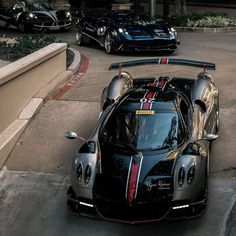 a black sports car parked on the side of a road next to other cars in front of a building