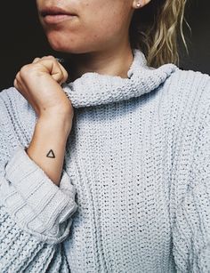 a woman with a small triangle tattoo on her left arm, wearing a blue sweater