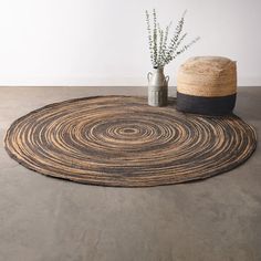 a round rug on the floor next to a vase with a plant in it and a straw hat