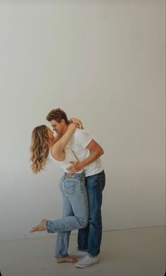 a man and woman are kissing in front of a white wall with their arms around each other