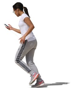 a woman in white shirt and grey pants walking with headphones on her ear while looking at cell phone