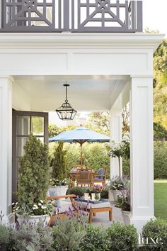 an outdoor living area with chairs, tables and umbrella in the middle of it is surrounded by greenery