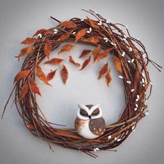 an owl figurine sitting on top of a wreath with branches and leaves around it