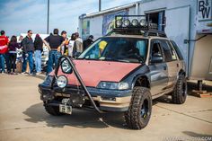 a car with an off - road bumper is parked in front of a group of people