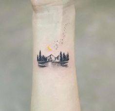 a small tattoo on the wrist of a person with trees and mountains in the background