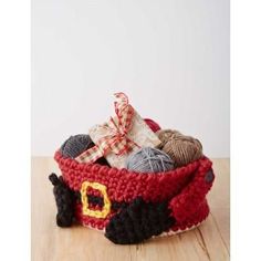 a crocheted basket filled with yarn and balls of yarn on top of a wooden table