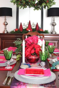 a dining room table set for christmas with red and green flowers in the centerpiece