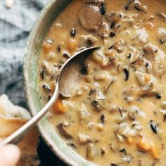 a person holding a spoon over a bowl of soup with mushrooms and carrots on the side