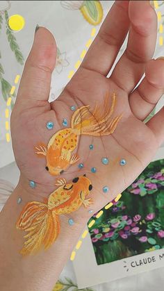 a person's hand with two gold fish painted on it and flowers in the background