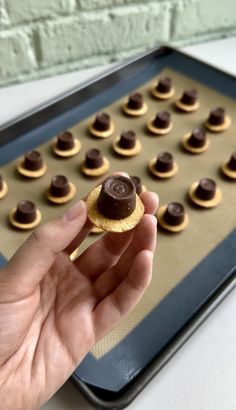 a hand holding a cookie in front of a baking sheet with chocolates on it