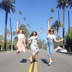 three women jumping in the air on a street with palm trees