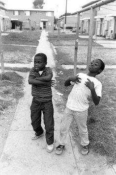 two young boys standing on a sidewalk next to a pole with their arms around each other