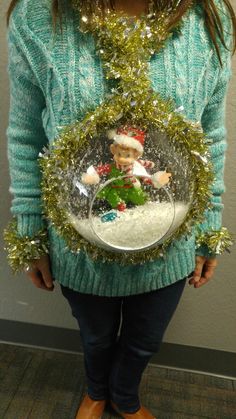 a woman is holding a snow globe with a santa clause on it and tinsel