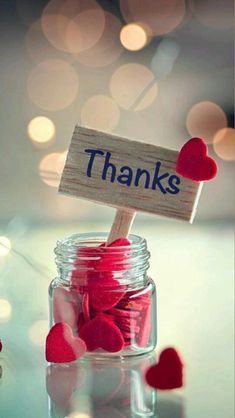 a jar filled with red hearts sitting on top of a table next to a sign that says thanks