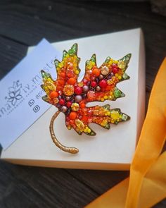 an autumn leaf brooch sits on top of a card next to a yellow ribbon