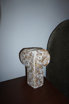 a vase sitting on top of a wooden table next to a black velvet headboard