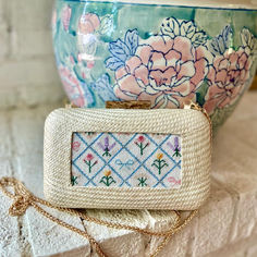 a white purse sitting on top of a counter next to a flowery potted plant