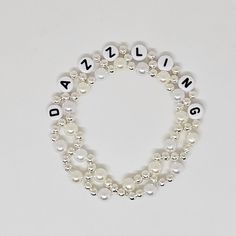 Visit bejeweledbangles.com for better pricing! This gorgeous bracelet is made of silver, white and pearl colored beads, "Dazzling" in white beads with black writing. This bracelet is so pretty and you will love wearing it proudly or gift it to a friend! Bracelet is made with elastic and various bead types. Minimalist Friendship Bracelet, Taylor Swift Lyric Bracelet Ideas, Personalized Silver Crystal Bracelet, Adjustable, Adjustable Pearl Bracelet With Silver Beads, Elegant Adjustable Charm Bracelet With Letter Beads, Adjustable Silver Pearl Bracelet For Friendship, Adjustable White Stretch Bracelet For Party, Personalized White Bracelets For Party, Party Jewelry Bracelet With Letter Beads