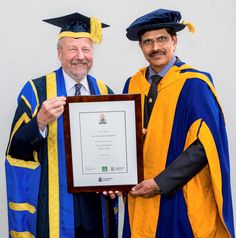 two men in graduation gowns holding an award plaque