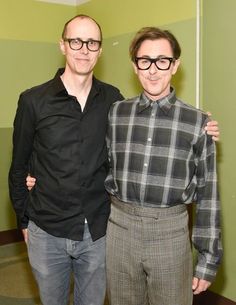 two men standing next to each other in front of a green wall