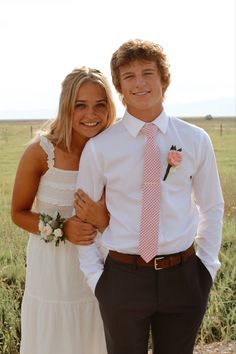 a young man and woman standing next to each other in front of an open field