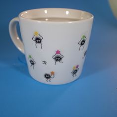 a white coffee cup with colorful designs on the outside and inside, sitting on a blue surface