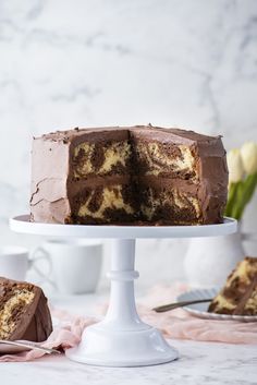 a chocolate cake on a white pedestal with one slice cut out and the other half eaten