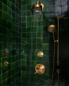 a green tiled shower with gold faucet and hand held shower head in the corner