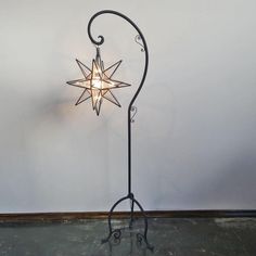 a star shaped light on a metal stand against a white wall with swirly arms