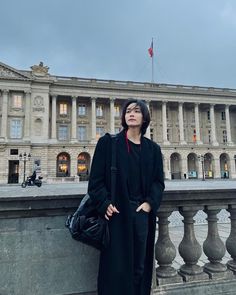 a woman leaning against a wall in front of a building with columns and a flag on it