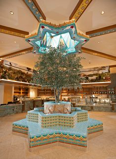 a tree in the middle of a lobby with an artistic design on it's ceiling