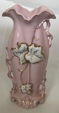 a pink vase with white flowers and gold trimmings sits on a white surface